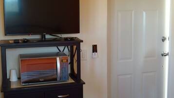 Habitación de hotel con televisor de pantalla plana sobre un soporte, dispensador de agua y una puerta.