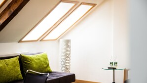 A modern living room with a sofa, green cushions, a glass table with bottles, and a tall white column. - TOP HOTEL ODELYA Basel (Basel)