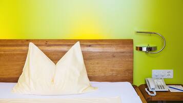 Une chambre d’hôtel avec une tête de lit en bois, un lit recouvert de draps blancs, une table de chevet avec un téléphone et un bloc-notes, et un mur vert.