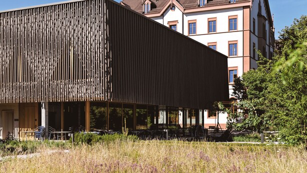 A modern building with a slatted facade and a traditional building in the background. - TOP HOTEL ODELYA Basel (Basel)