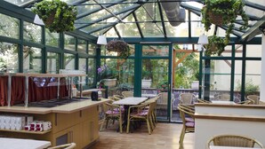 A greenhouse with tables and chairs, a kitchen area, and hanging plants. - Anna Hotel (Prague)