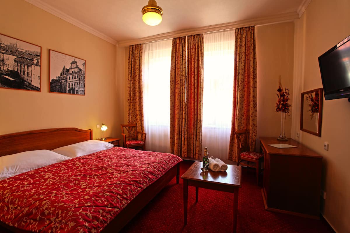 A hotel room with a large bed, a desk, a chair, a TV, and two framed pictures on the wall.