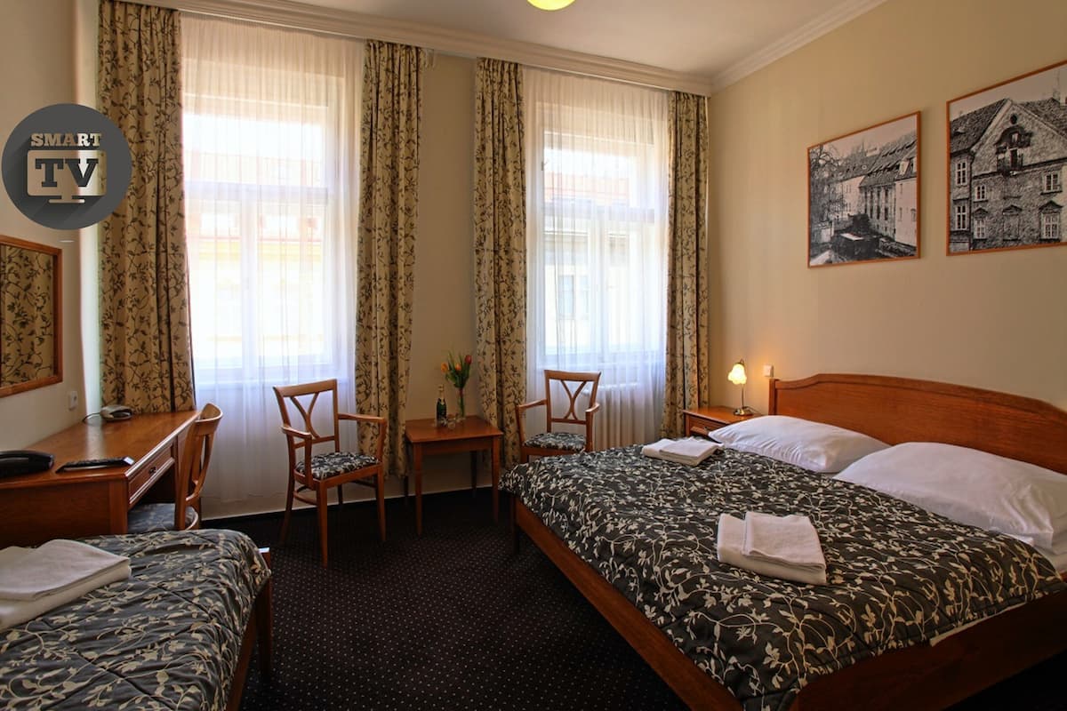 A hotel room with two single beds, a desk with a chair, a small table with a vase of flowers, and two framed pictures on the wall.