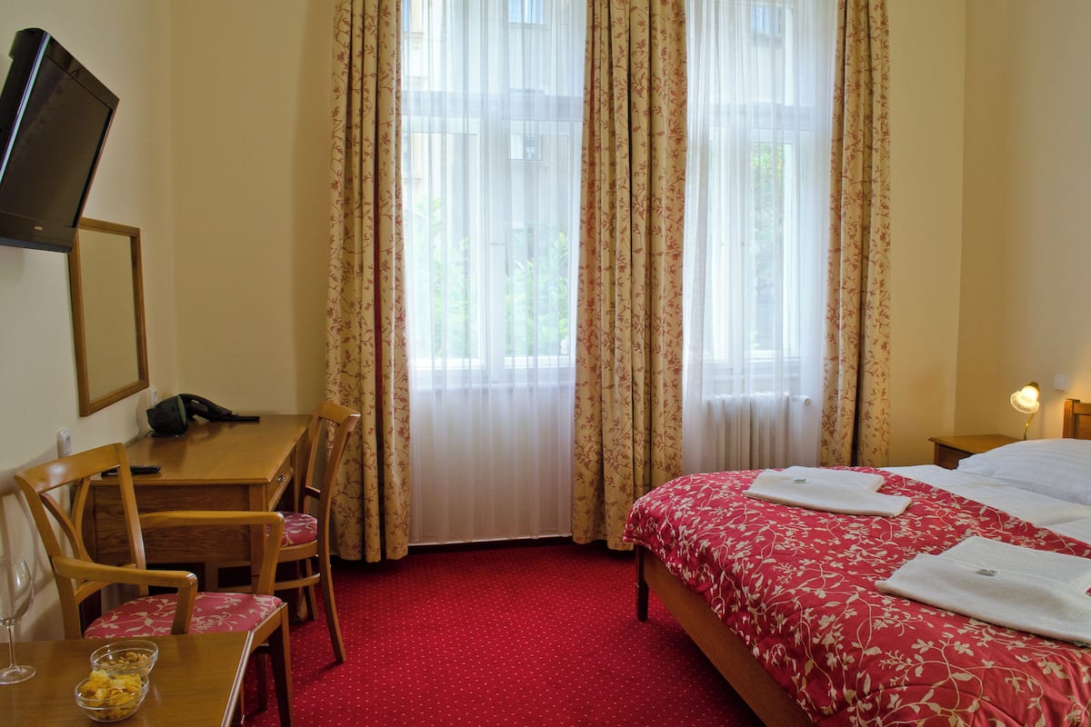 A hotel room with a bed, a desk, a chair, a television, and a window with curtains.