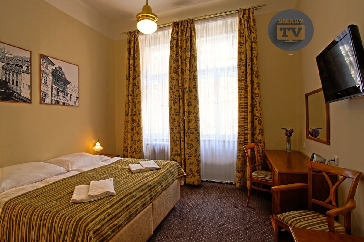A hotel room with a bed, a desk, a chair, a TV, and a window with curtains.