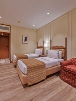 Ein Hotelzimmer mit zwei Betten, einem roten Sessel, einem Nachttisch mit Lampe sowie einem gerahmten Bild an der Wand.
