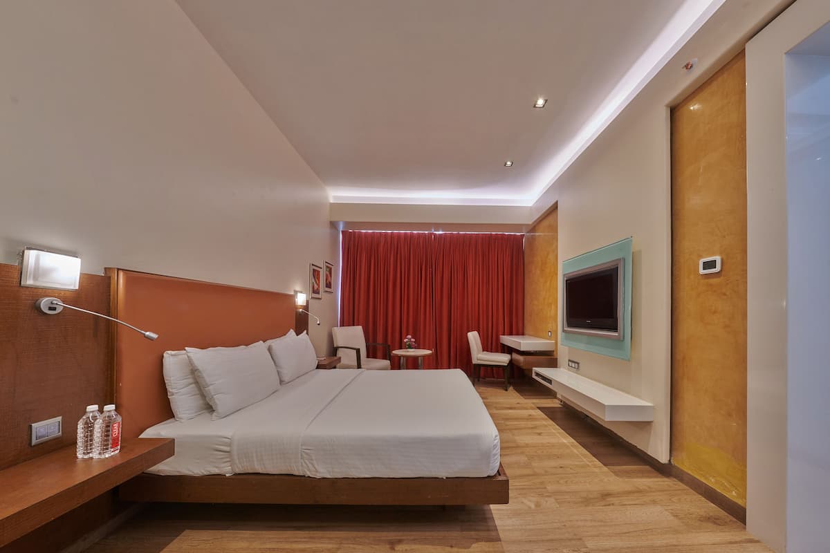 Una habitación de hotel moderna con una cama grande, un escritorio, un televisor y una cortina roja.