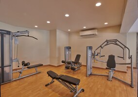 Een sportschool met diverse fitnessapparaten, banken en een airconditioningunit aan het plafond.