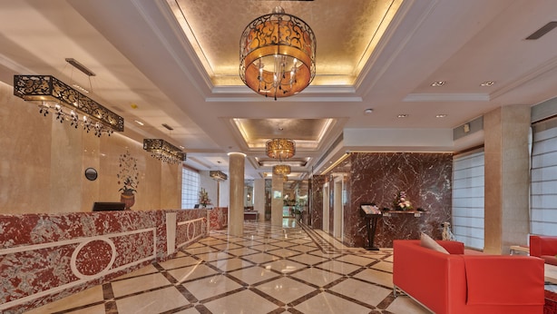 A spacious lobby with a marble floor, a reception desk, and a red seating area.