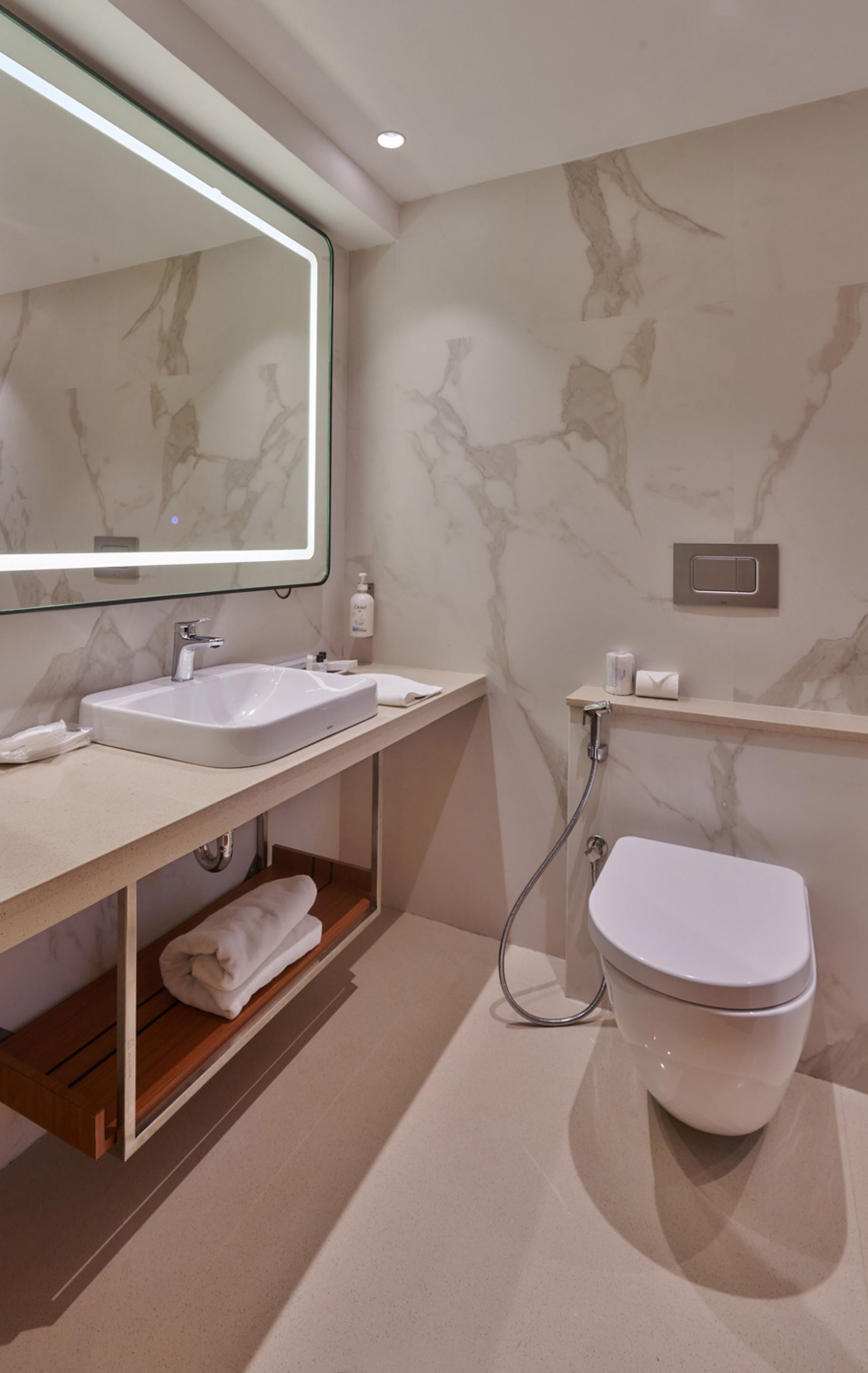 Un bany modern amb paret de marbre, un mirall gran, un lavabo, un vàter i una dutxa.