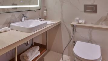 Un bany modern amb paret de marbre, un mirall gran, un lavabo, un vàter i una dutxa.
