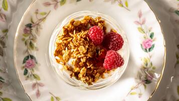 Un bol de granola garni de framboises, présenté sur une assiette à motifs floraux.