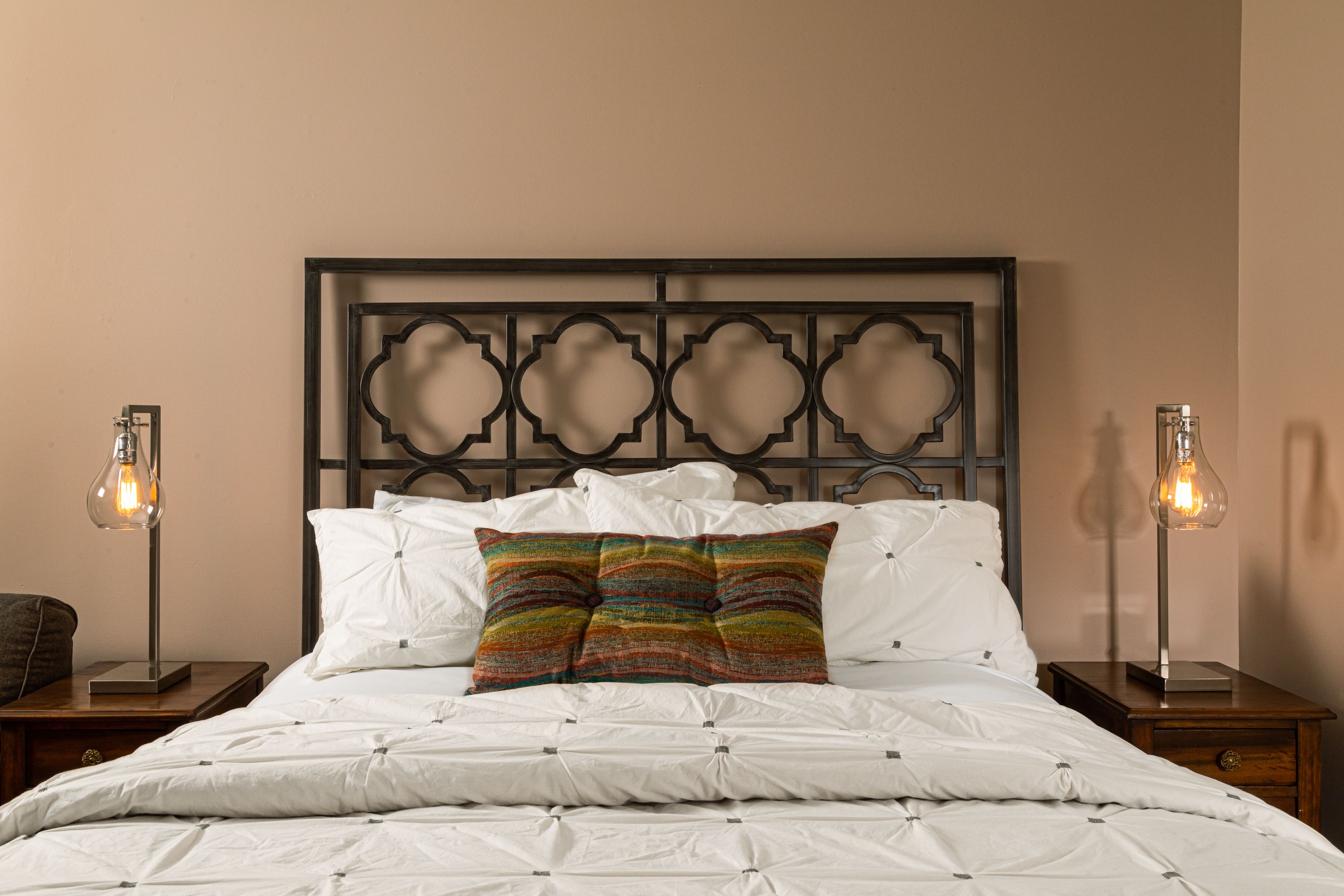 A neatly made bed with white linens and a colorful striped pillow, flanked by two bedside tables with lamps.