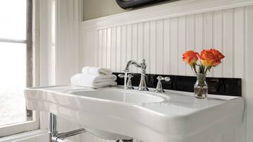 A white bathroom sink with two faucets, a mirror above it, and a vase with roses on the countertop.