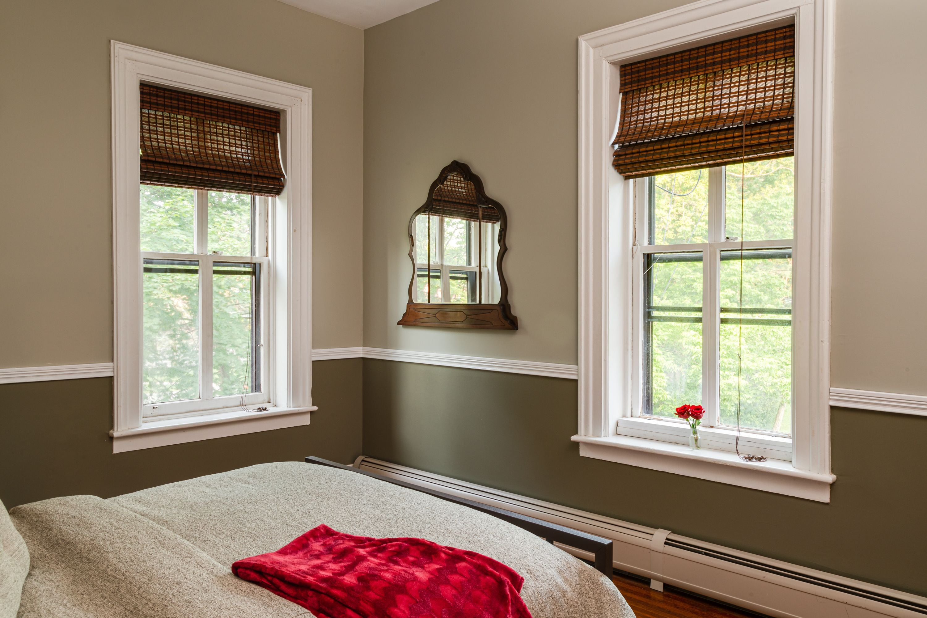 A bedroom with two windows, a radiator, and a mirror.