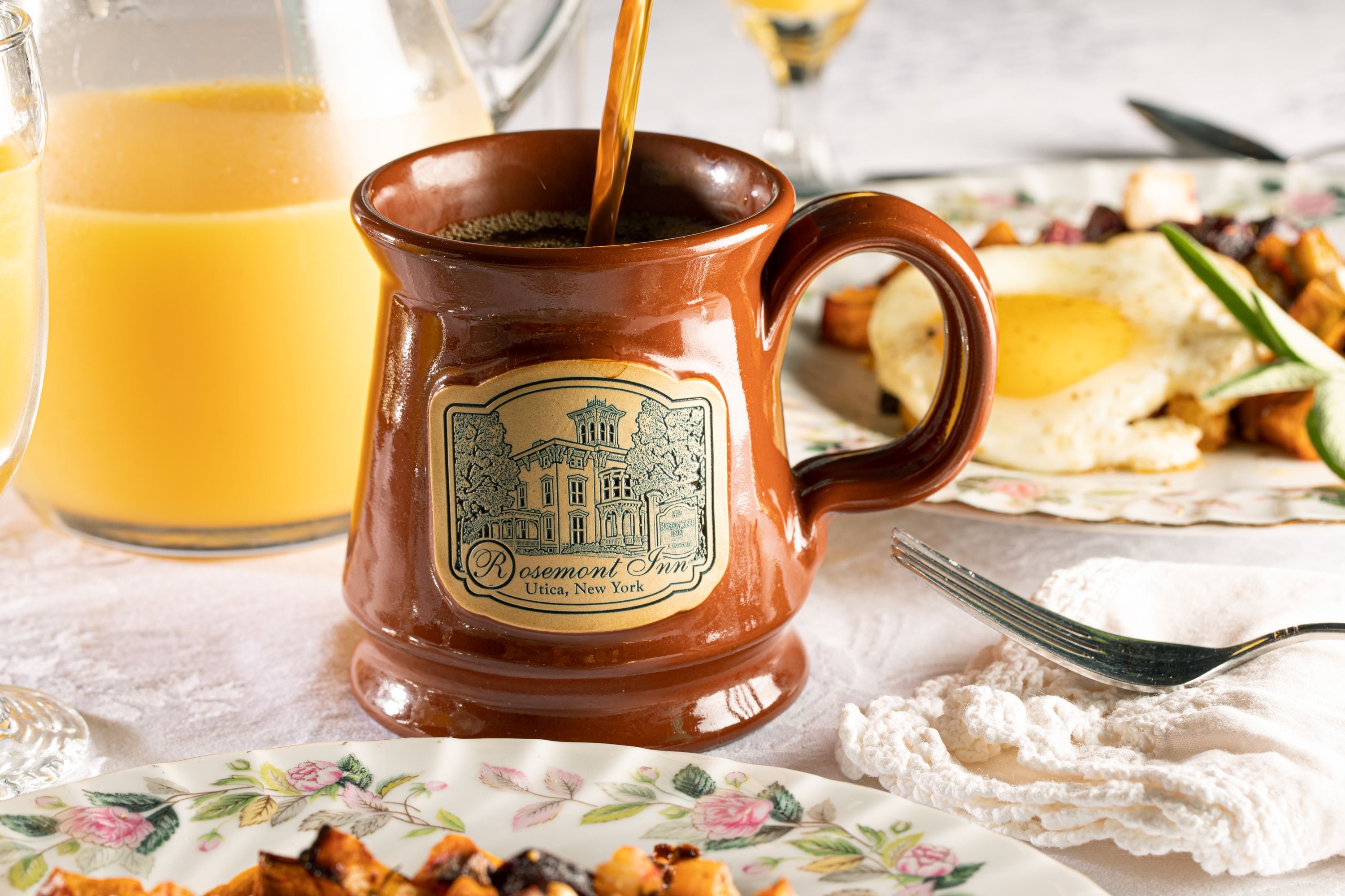 Una taza de cerámica con asa, un vaso de jugo de naranja y un plato con alimentos.