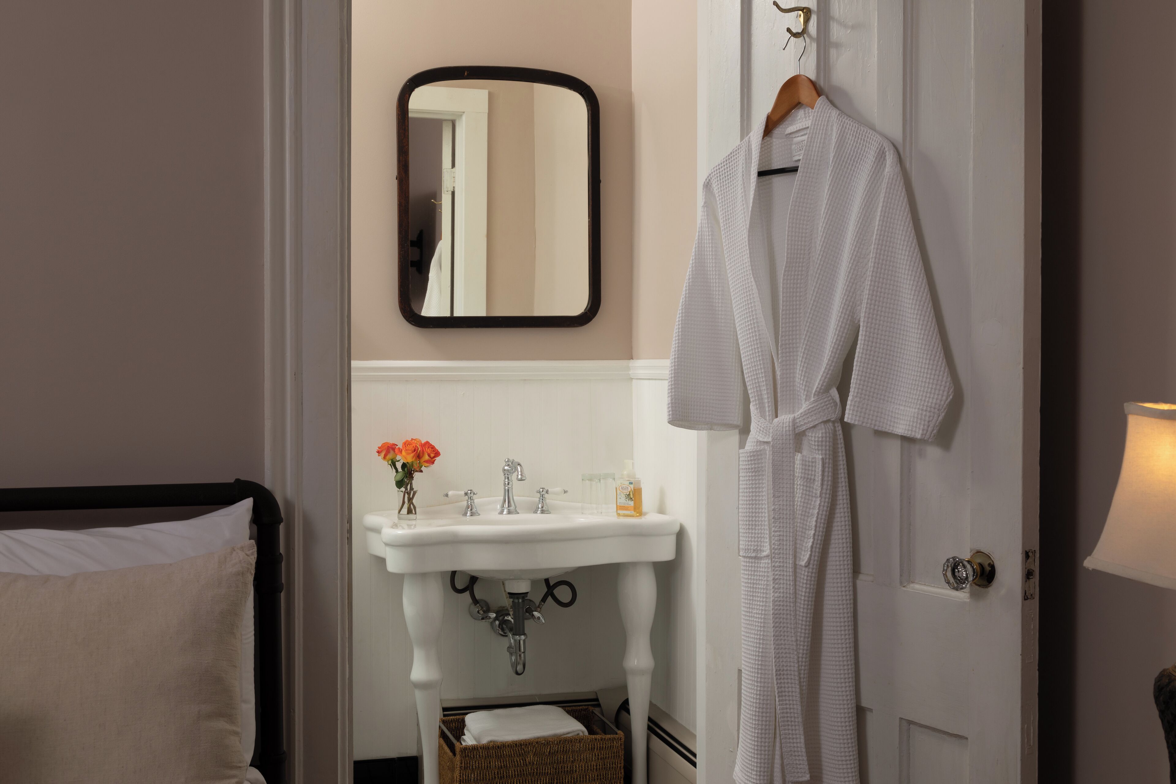 A bathroom with a white sink, mirror, and a robe hanging on the door.
