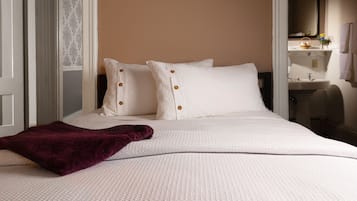 Un lit bien fait, avec une couette blanche et deux oreillers, un plaid violet et une tête de lit blanche.