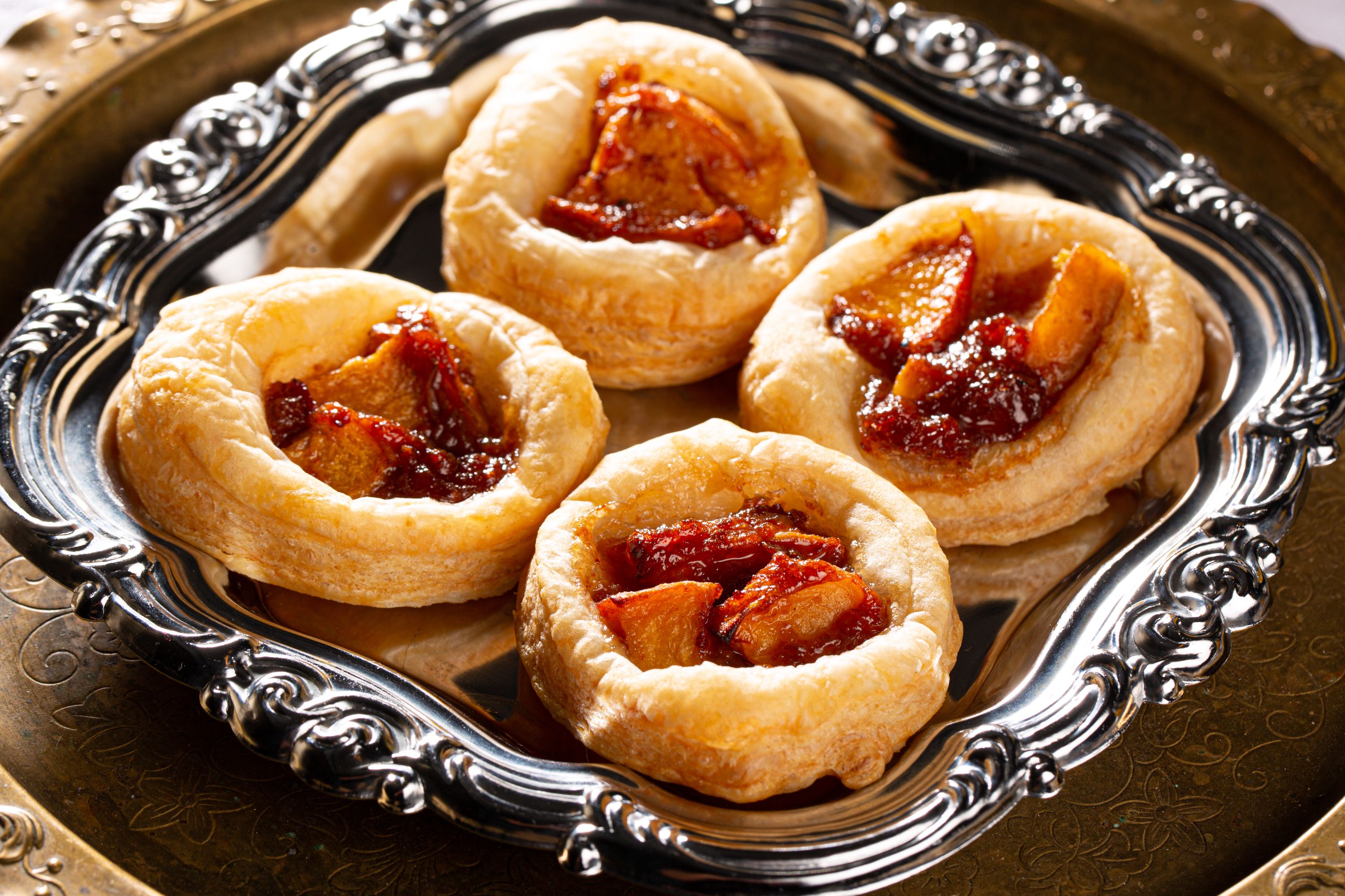 Four fruit tarts on an ornate silver tray.