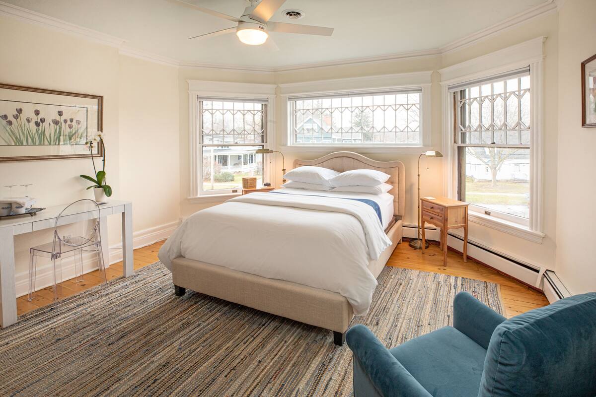 A bedroom with a bed, a desk, and two windows.
