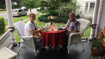 Two people seated at a round table with a red tablecloth on a porch.