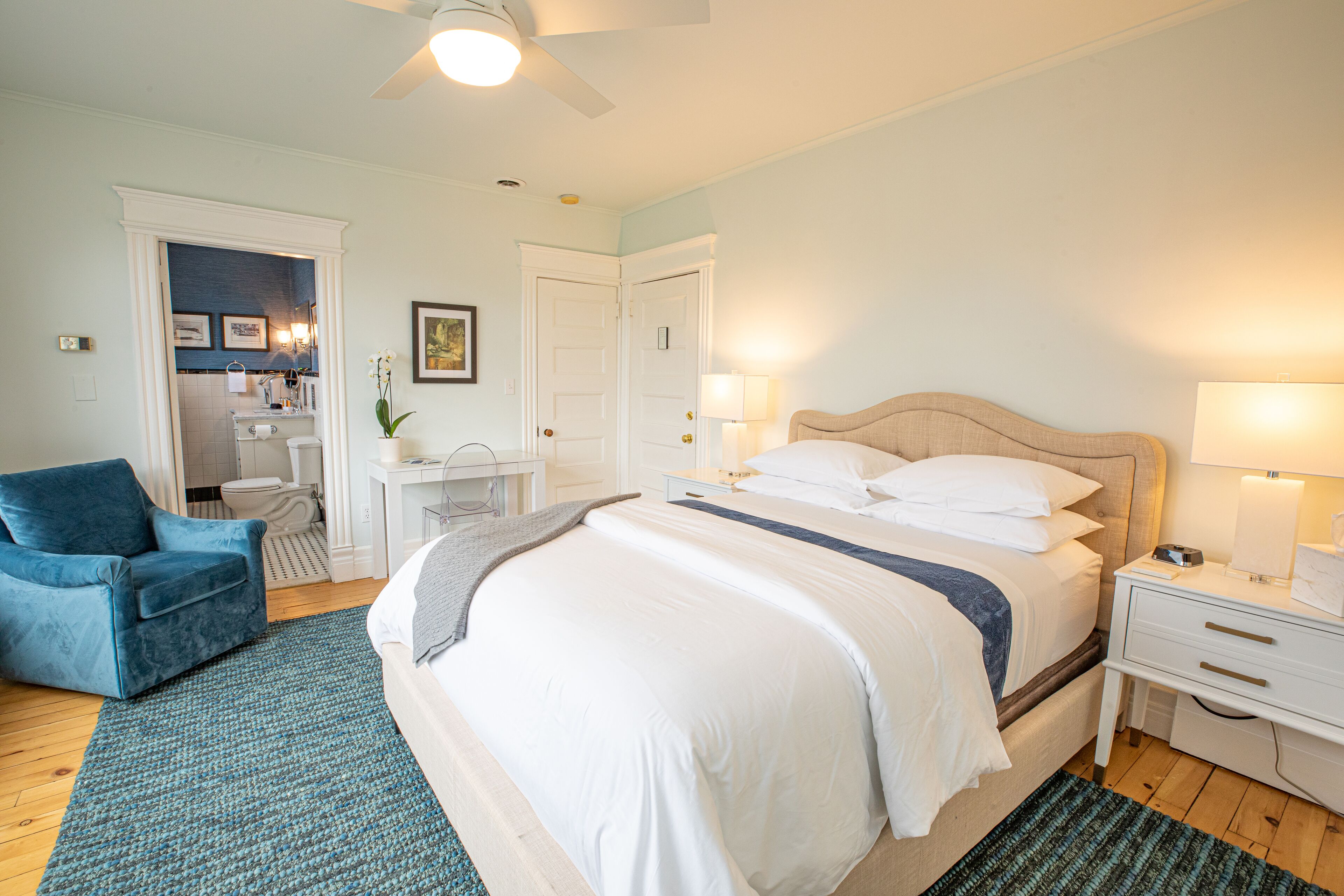 A bedroom with a bed, bedside tables, a chair, and a bathroom visible through an open door.