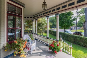 A covered porch with a white chair, red flowers, and a dog. - 2W Lake (Skaneateles)