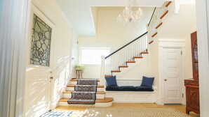 Un escalier recouvert d’une moquette à motifs, un banc avec des coussins et un lustre.