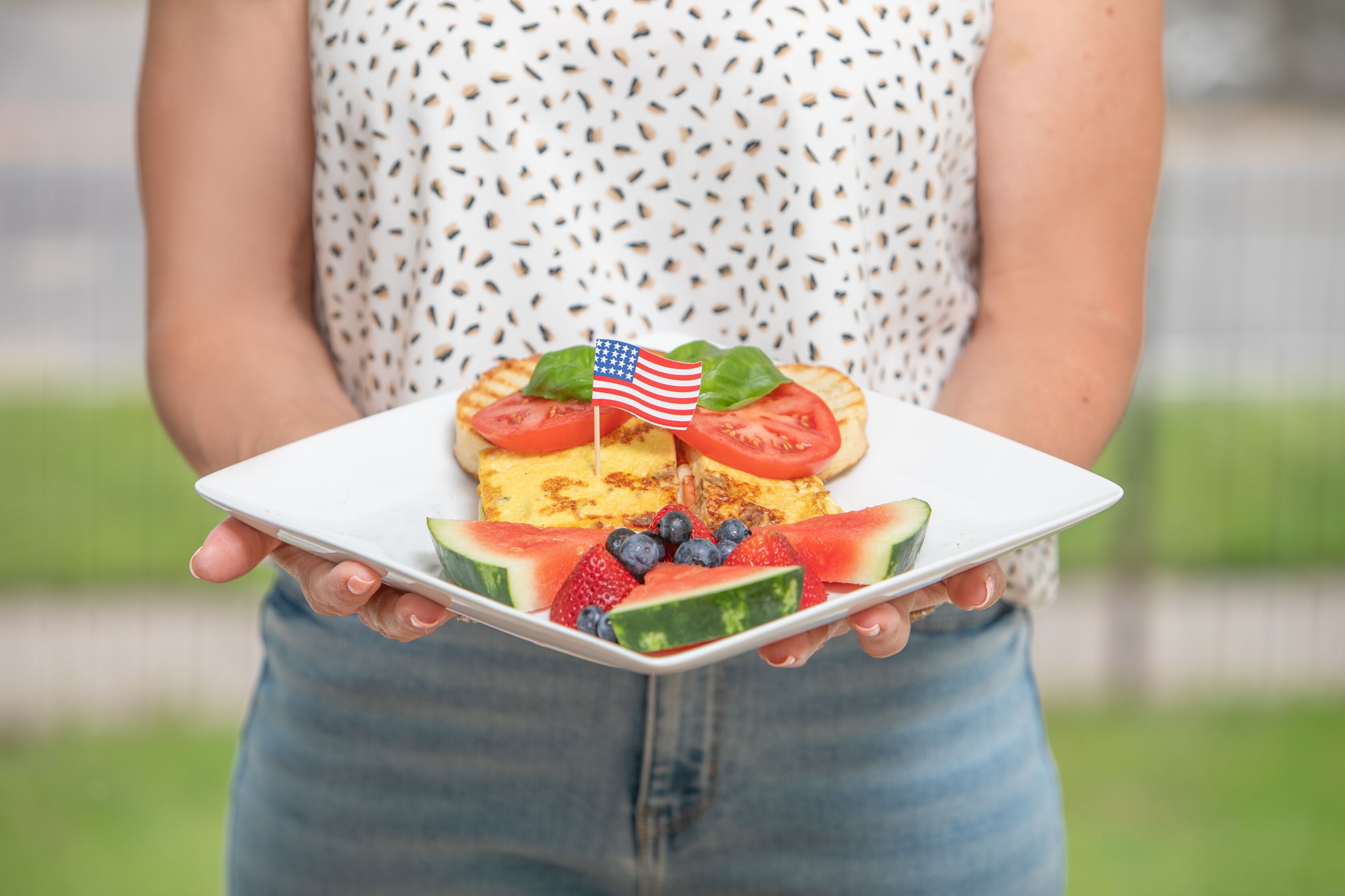 Une personne tenant une assiette blanche sur laquelle on voit une part de gâteau, des tomates, des myrtilles, des fraises et une tranche de pastèque.