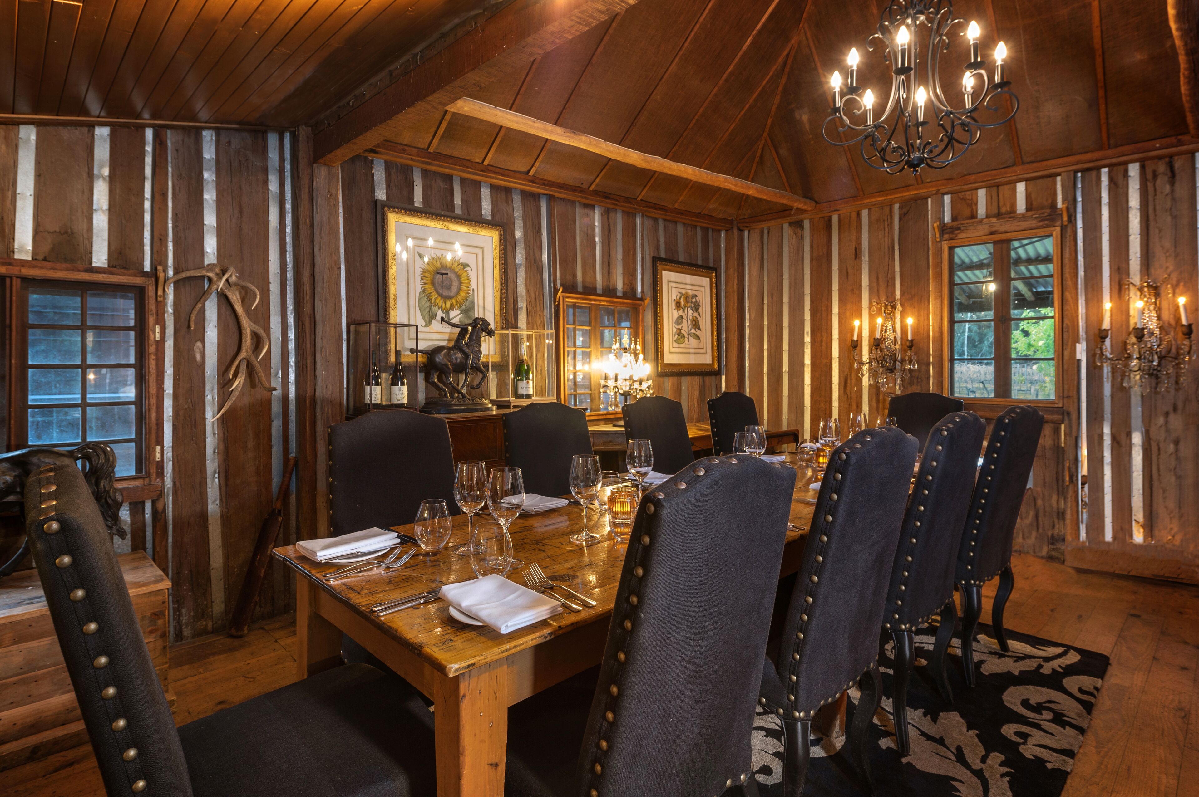 A dining room with a wooden table set for six, surrounded by upholstered chairs with metal studs.