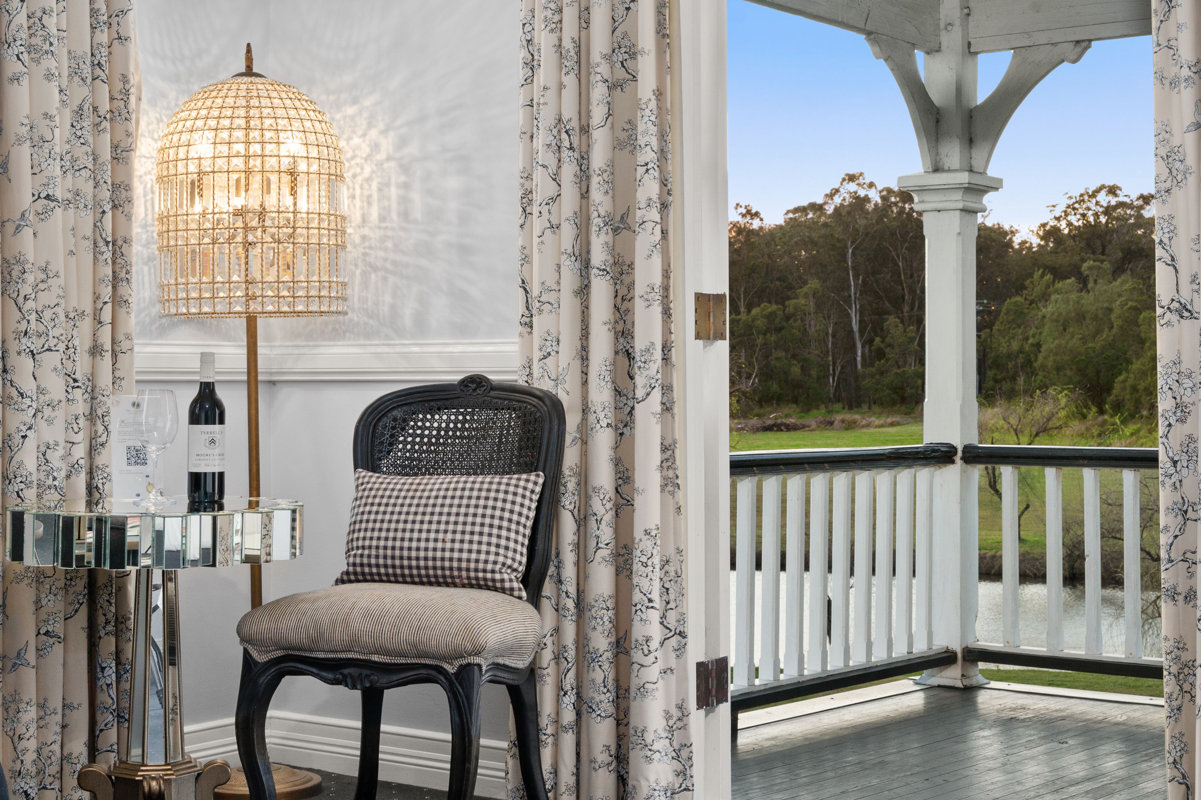 A room with a checkered chair, a glass table with a bottle, and a decorative lamp.