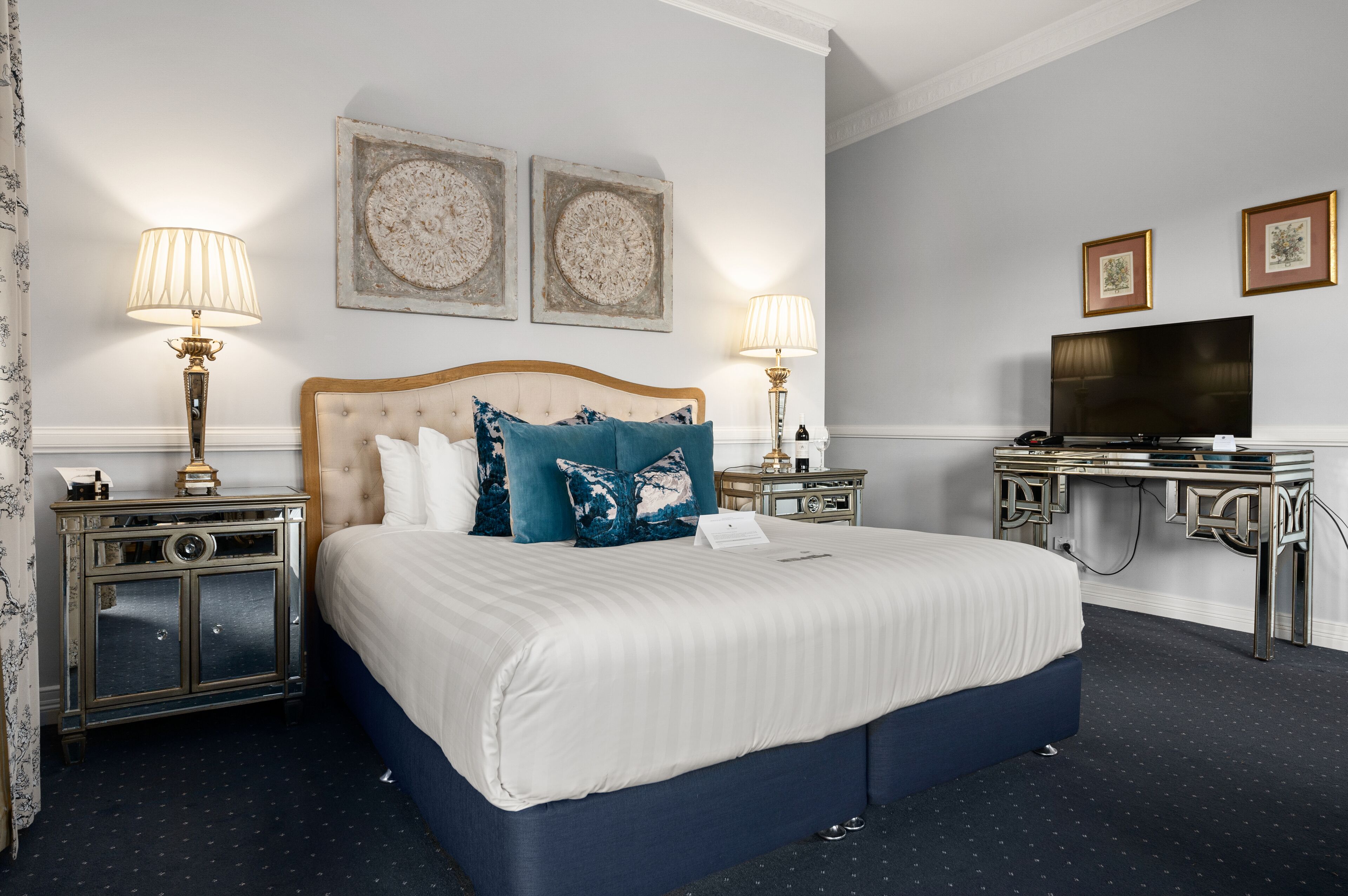 A hotel room with a large bed, two bedside tables with lamps, a flat-screen TV, and artwork on the walls.