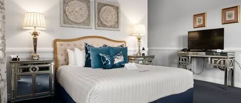 A hotel room with a large bed, two bedside tables with lamps, a flat-screen TV, and artwork on the walls.