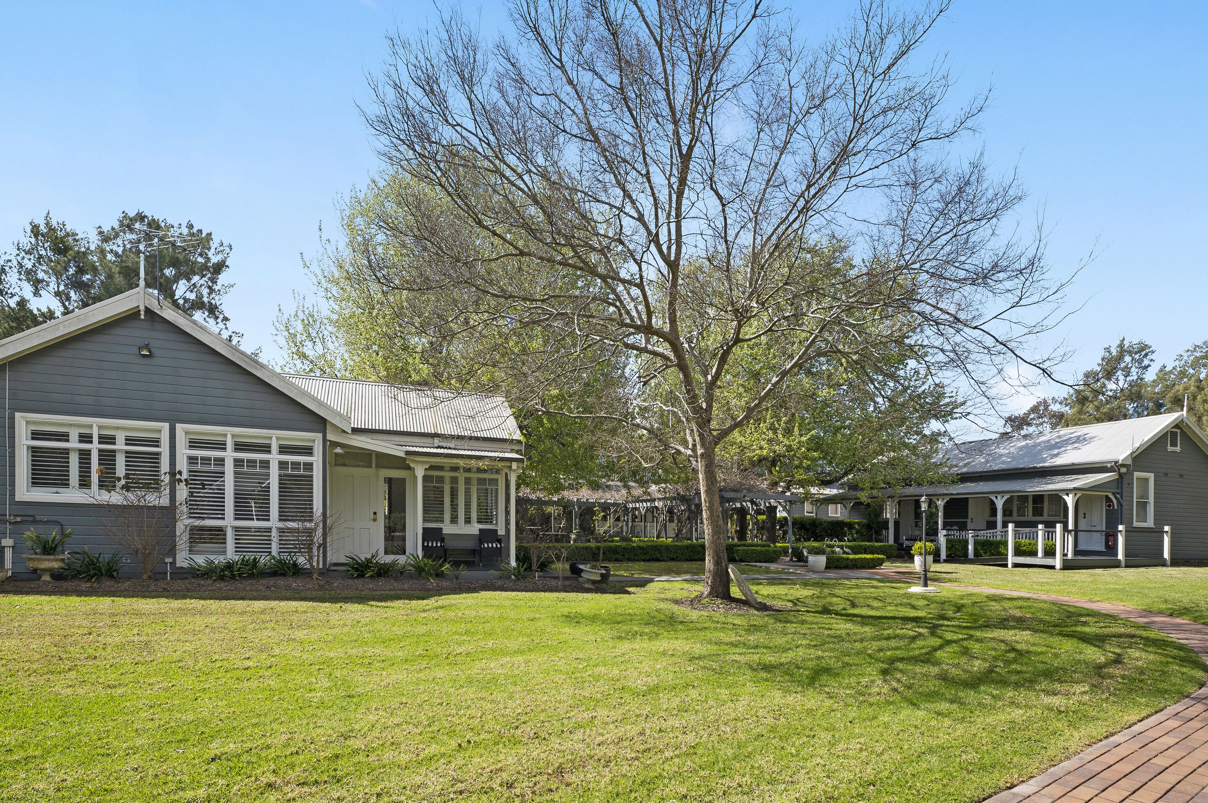 A two-story house with a porch and a large tree in the front yard.