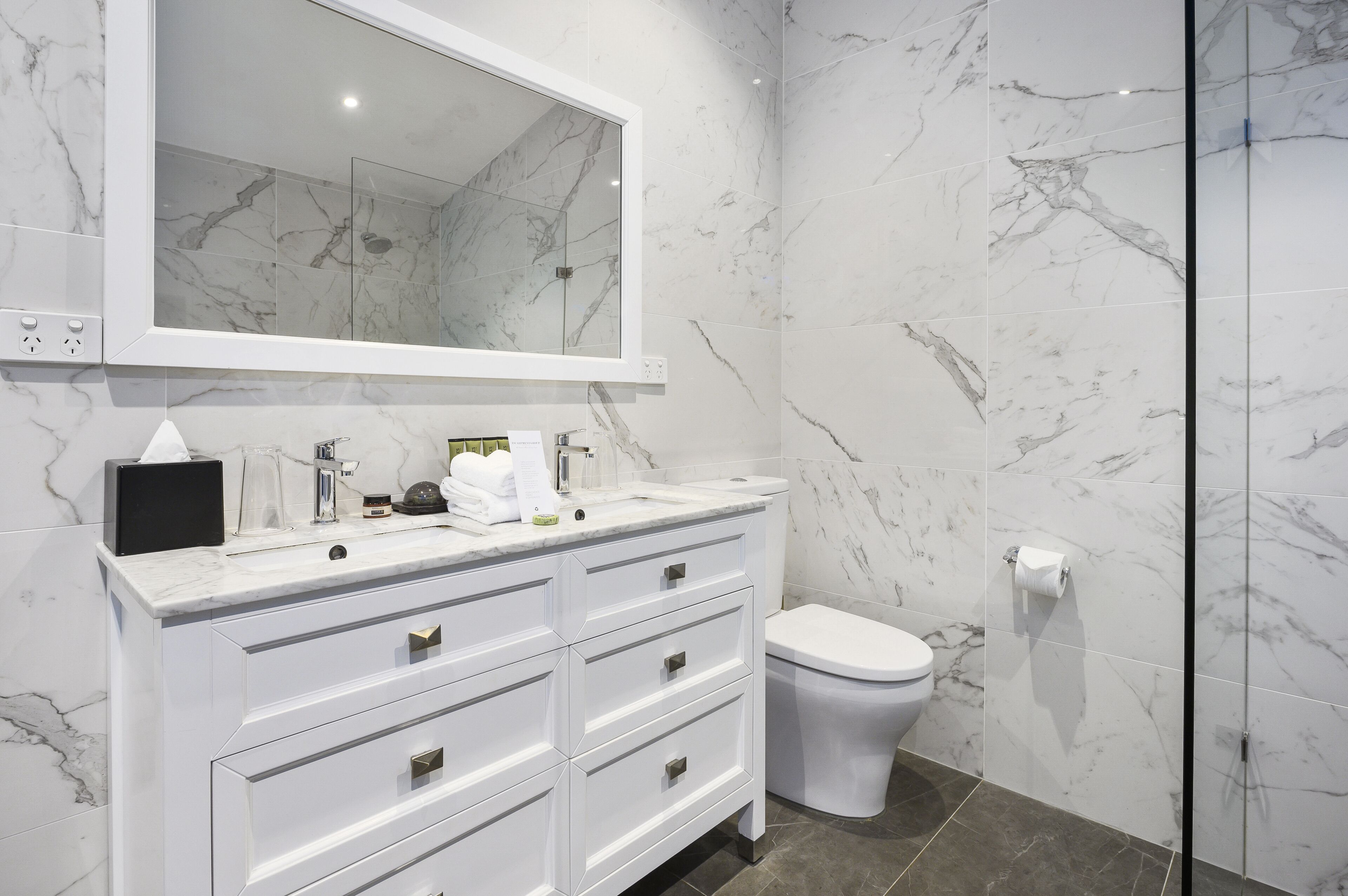 Un baño moderno con tocador de mármol, inodoro y cabina de ducha de vidrio.