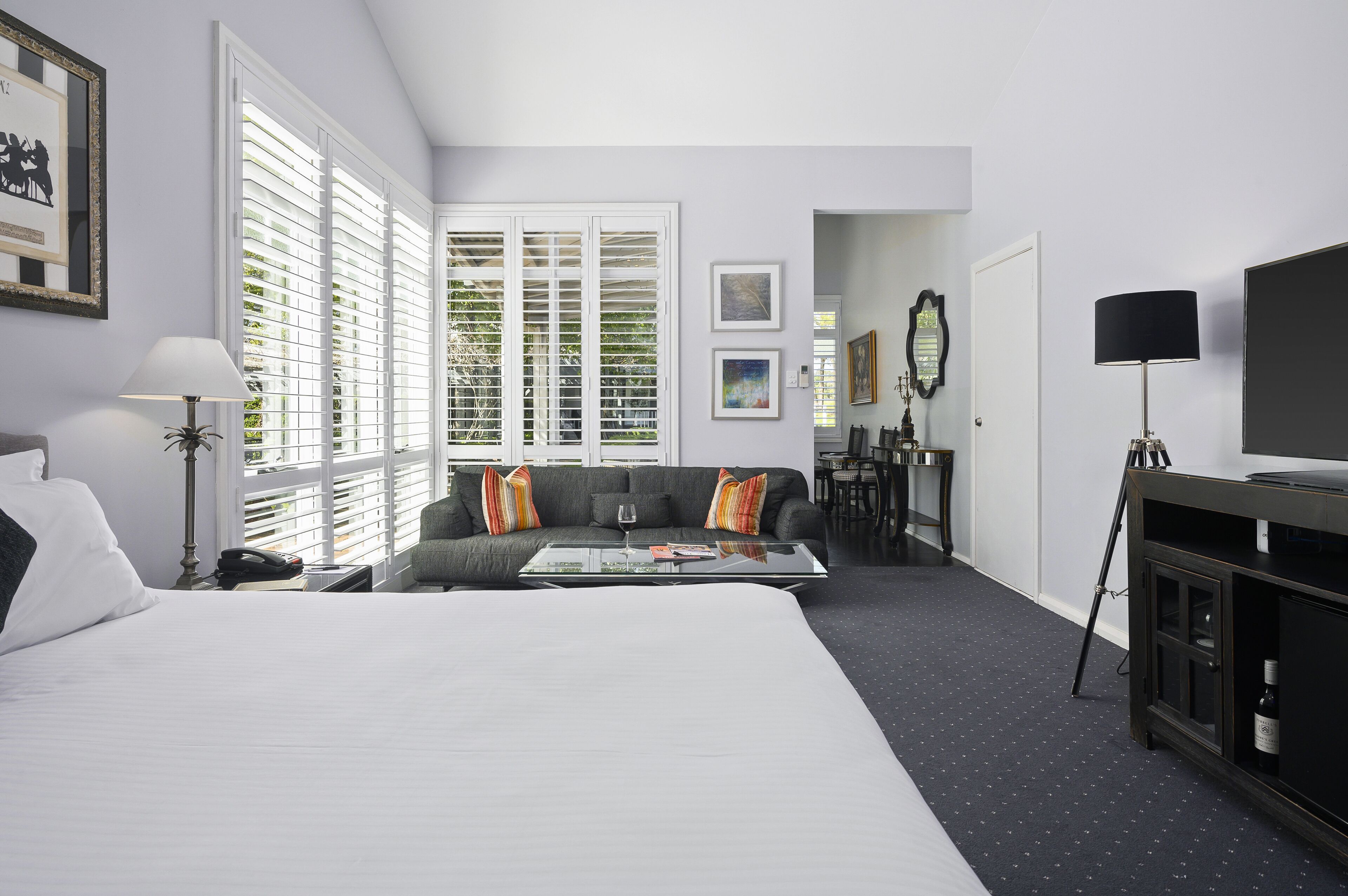 A hotel room with a large bed, a sofa, a glass coffee table, and a TV stand.