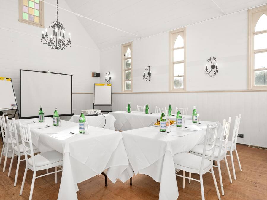 A conference room with white tables, chairs, a projector, and a screen.