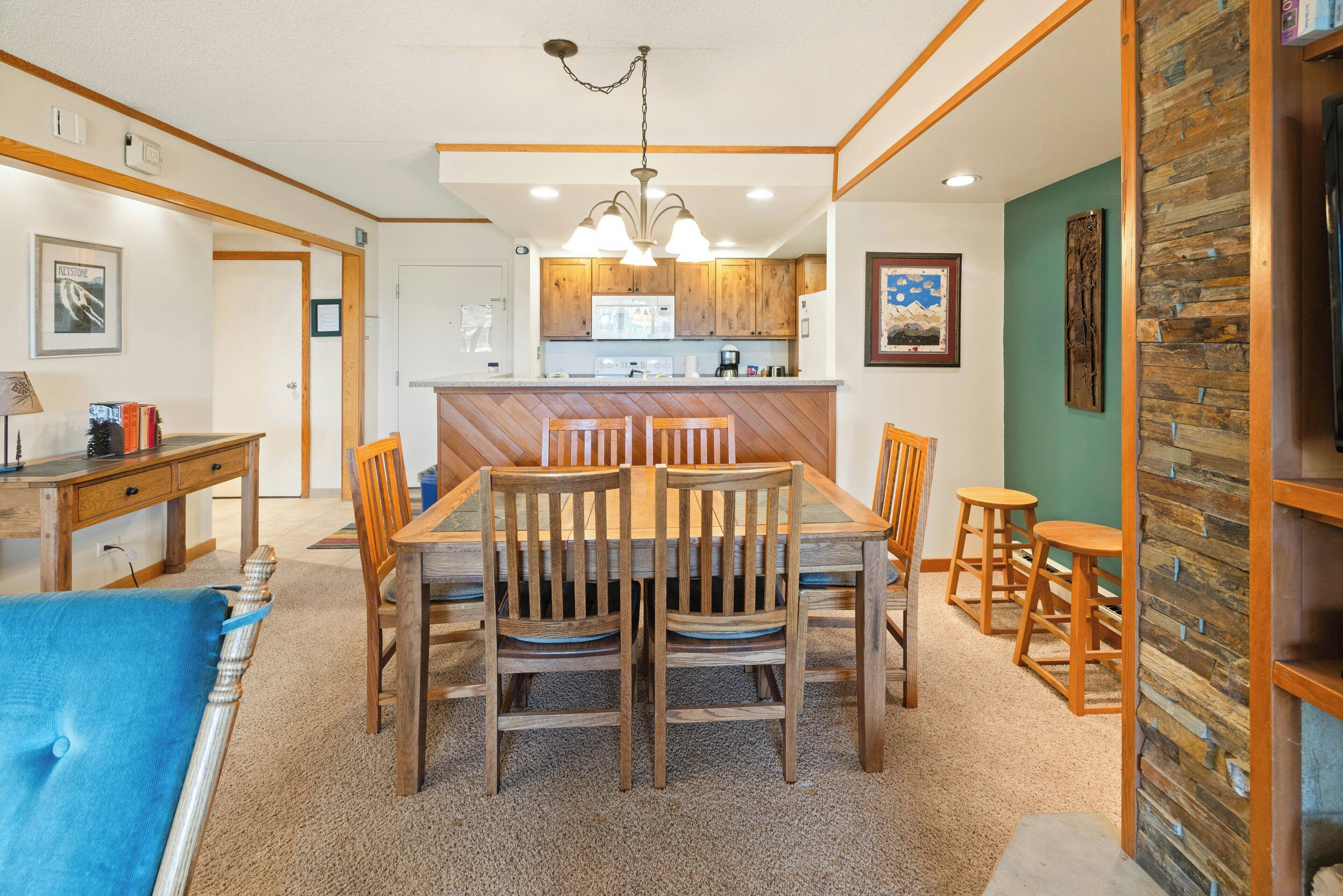 A dining area with a wooden table and chairs, a kitchen in the background, and a herringbone-patterned wall.