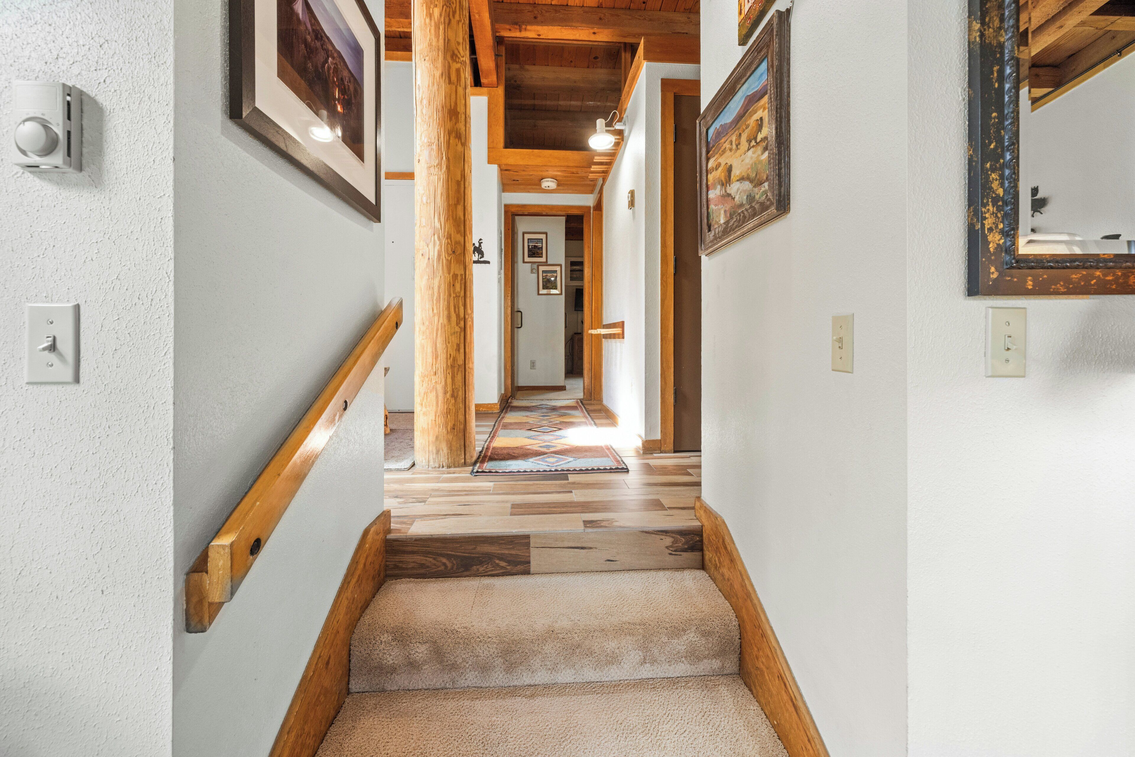 A wooden staircase with a carpeted landing, white walls, and framed pictures on the walls.