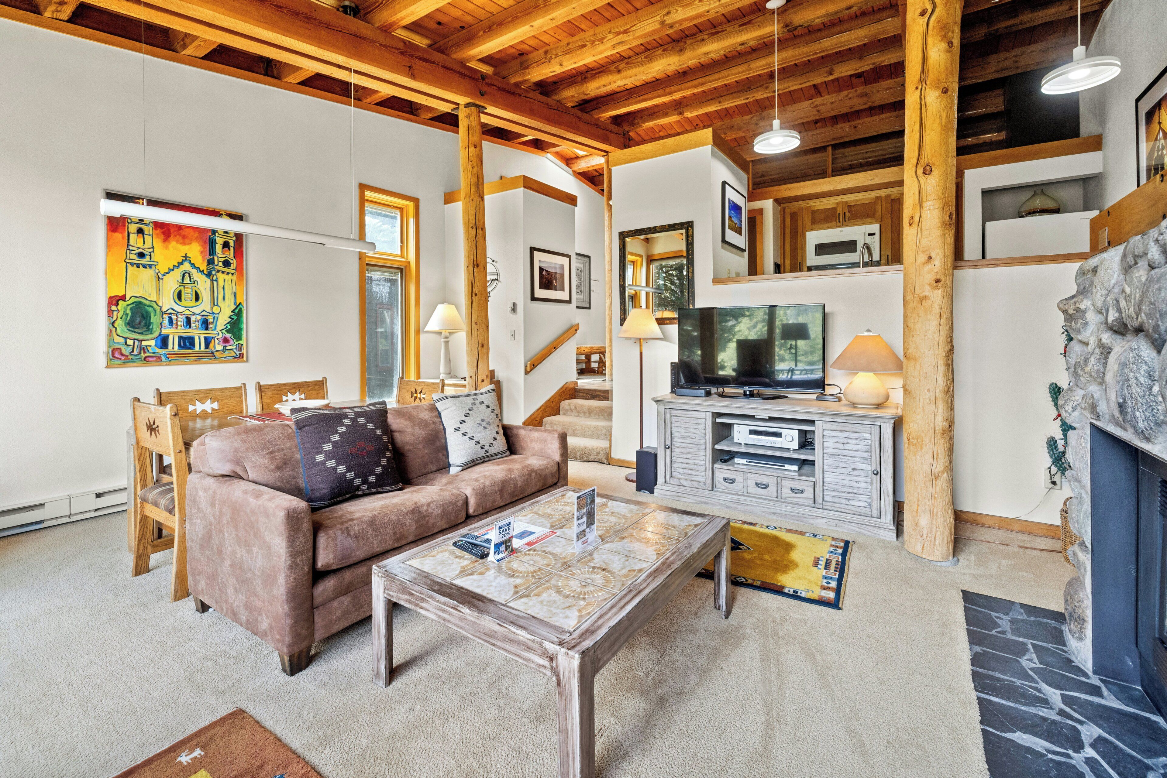 A cozy living room with a wooden ceiling, a brown sofa, a coffee table, and a stone fireplace.