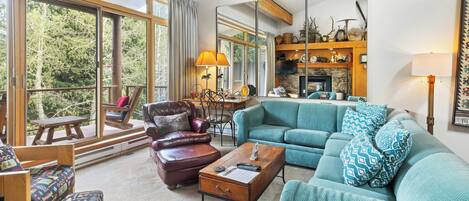 Un salón acogedor con un sofá color turquesa, una mesa de centro de madera y un sillón de cuero. Hay una chimenea con revestimiento de piedra y un espejo encima.