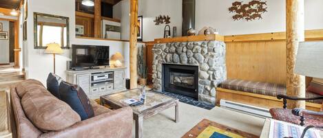 A cozy living room with a stone fireplace, wooden beams, a television, and comfortable seating.
