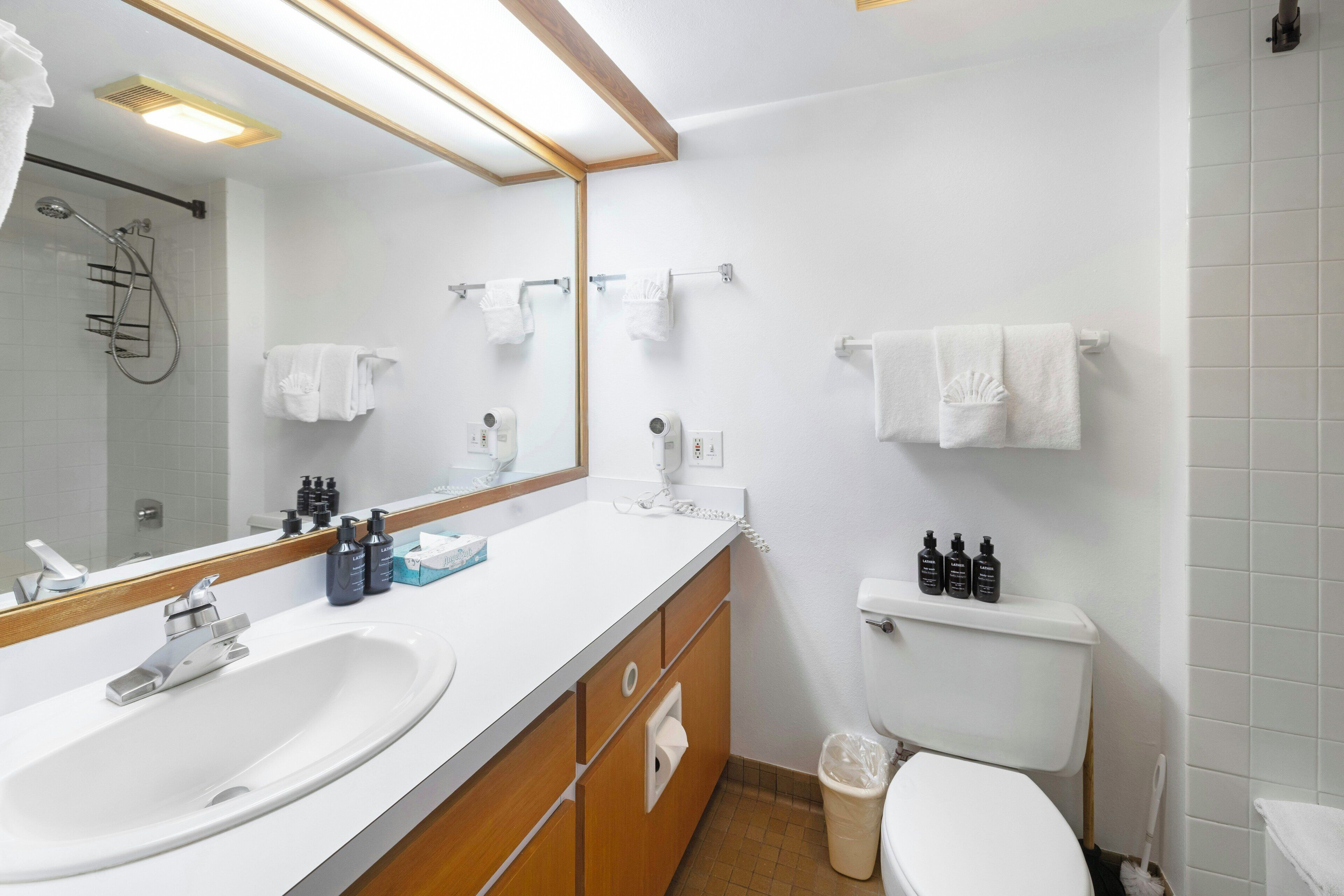 A modern bathroom with a white sink, mirror, and toilet. There are towels hanging on the wall and toiletries on the counter.