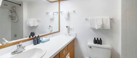 A modern bathroom with a white sink, mirror, and toilet. There are towels hanging on the wall and toiletries on the counter.