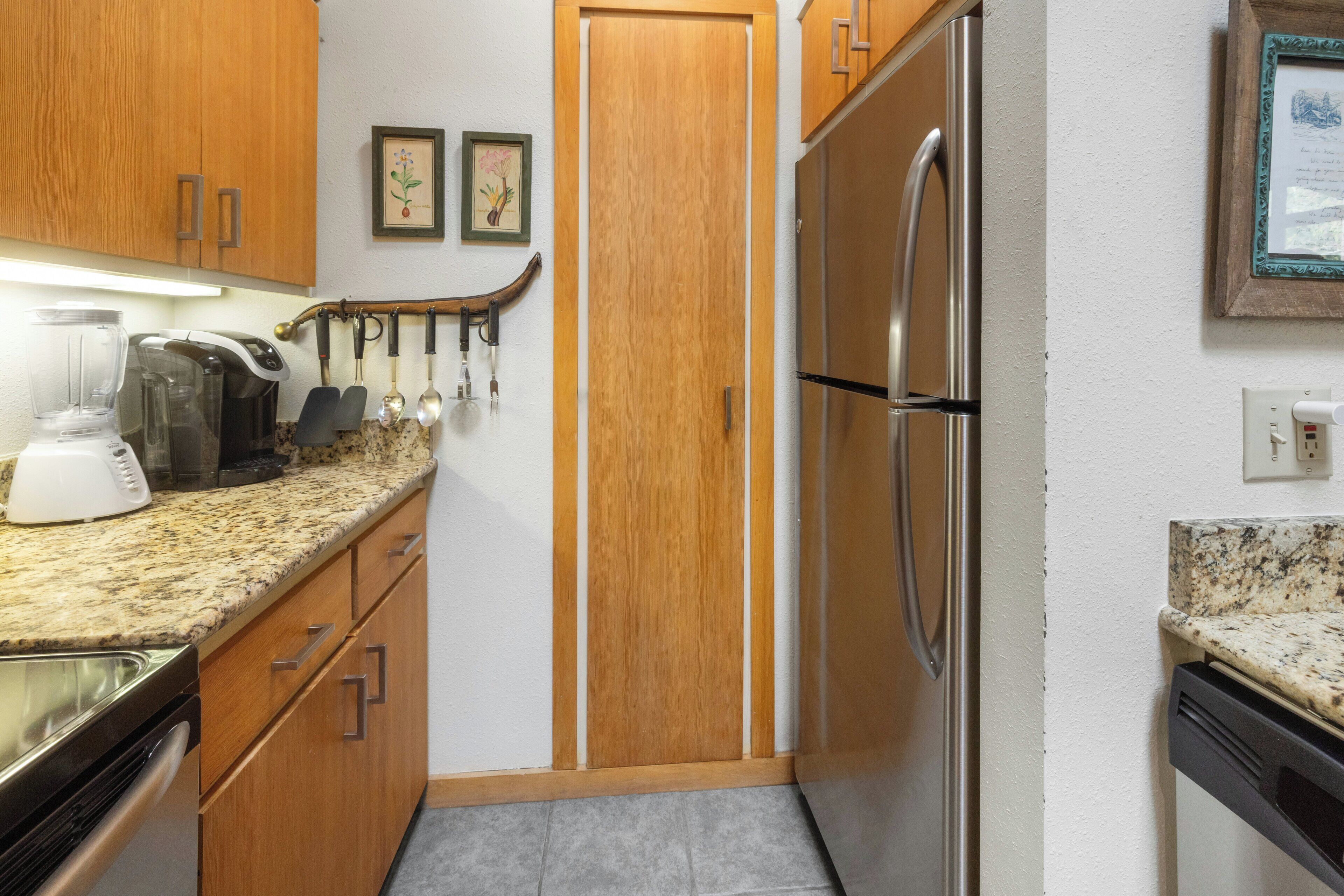 Cocina compacta con armarios de madera, un refrigerador de acero inoxidable, una cafetera y una licuadora.