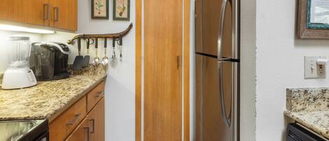 Cocina compacta con armarios de madera, un refrigerador de acero inoxidable, una cafetera y una licuadora.