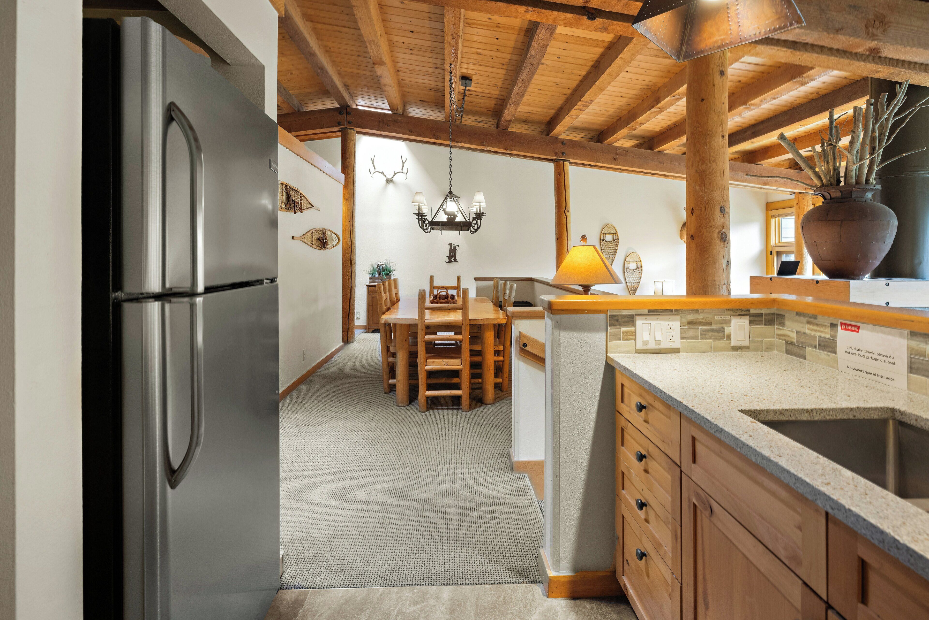 Una cucina moderna con mobili in legno, un frigorifero in acciaio inossidabile, un'area pranzo con tavolo e sedie in legno e un lampadario.