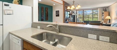A kitchen with a granite countertop, stainless steel sink, wooden cabinets, and a dishwasher.