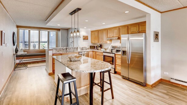 A spacious kitchen with a large island, wooden cabinets, stainless steel appliances, and a view of the outdoors through large windows. - Evergreen Condominiums by Vail Resorts (Keystone)