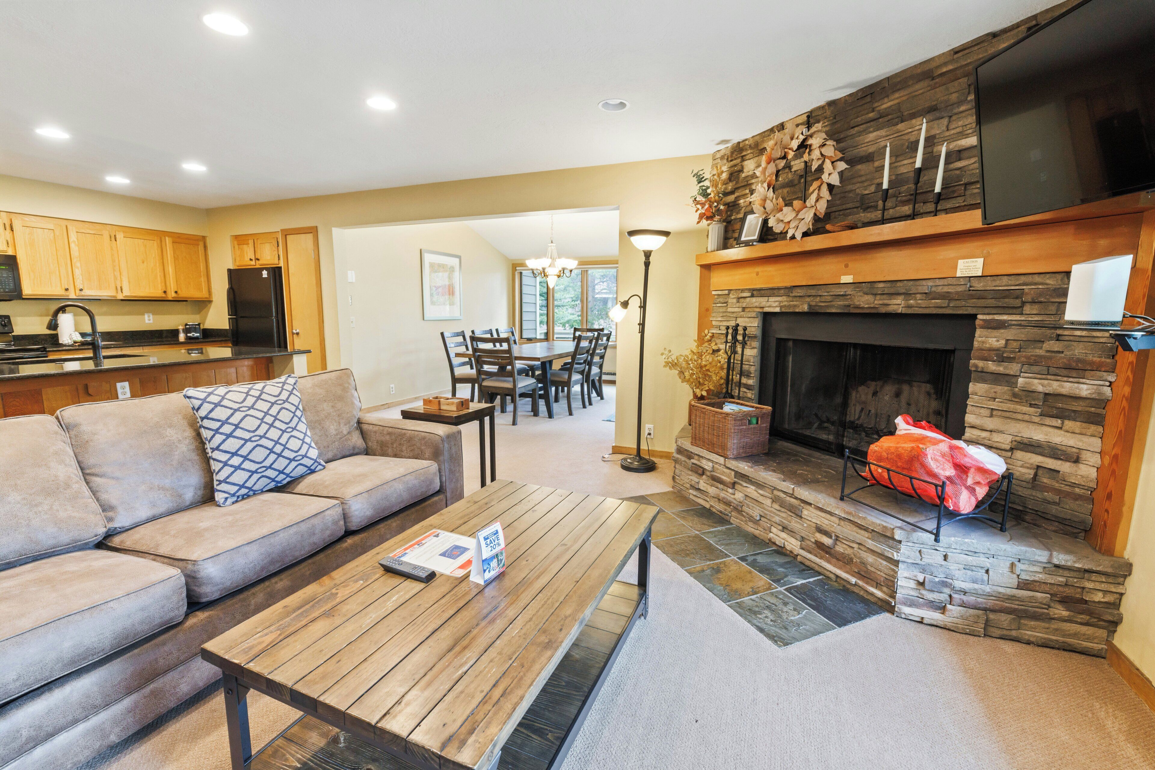 A modern living room with a fireplace, a dining area, and a kitchen.